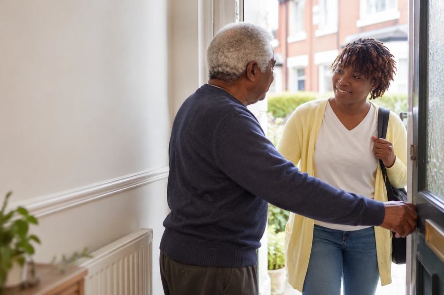 An older man welcoming his carer in at his front door